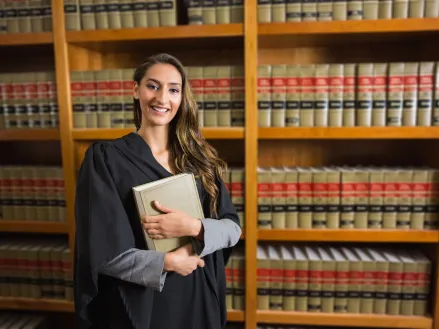 Law student in graduate robe looking at camera in the law library at a university