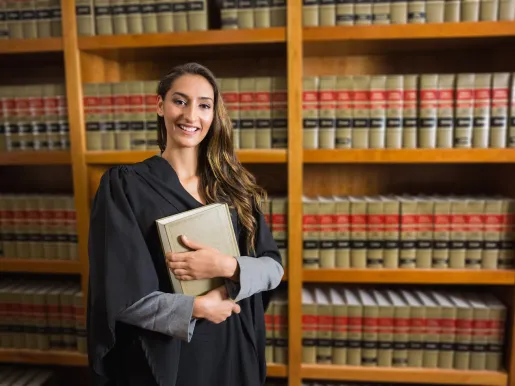 Law student in graduate robe looking at camera in the law library at a university