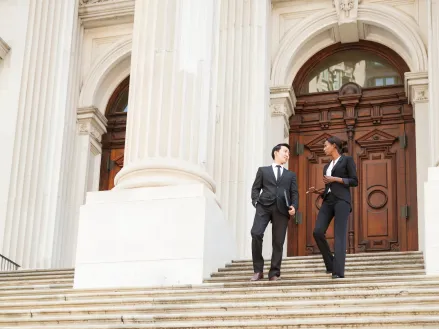 Man and woman dressed in suits walking down steps of a courthouse building